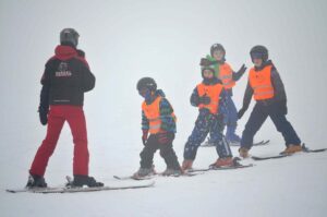 Skupina dětí s instruktorkou na lyžích.